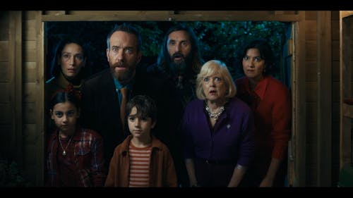 A group of seven people from three generations crowds in a doorway staring amazed with their eyes wide and mouths open at something inside.