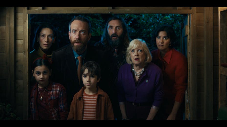 A group of seven people from three generations crowds in a doorway staring amazed with their eyes wide and mouths open at something inside.