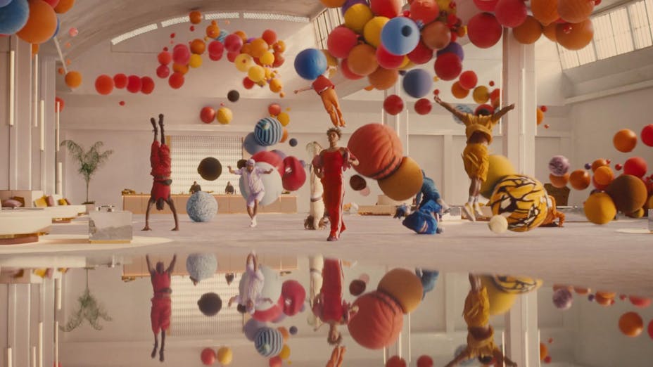 Large white indoor scene full of colored balls, balloons and people jumping, all in red, yellow, and blue.