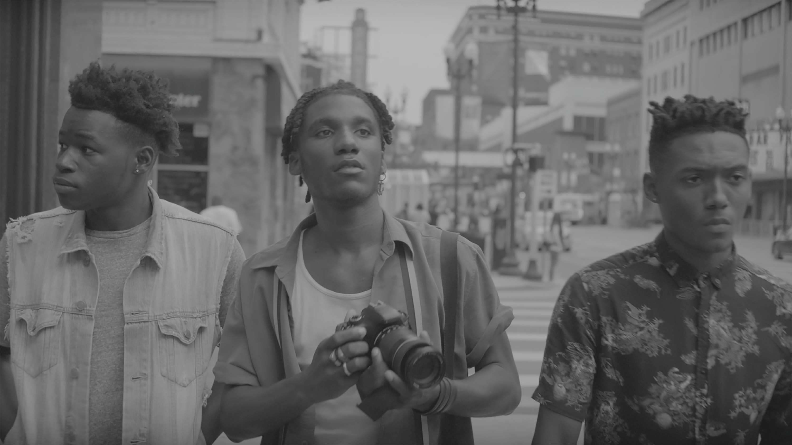 Three young men walk on a Minneapolis crosswalk. The middle figure holds a camera.