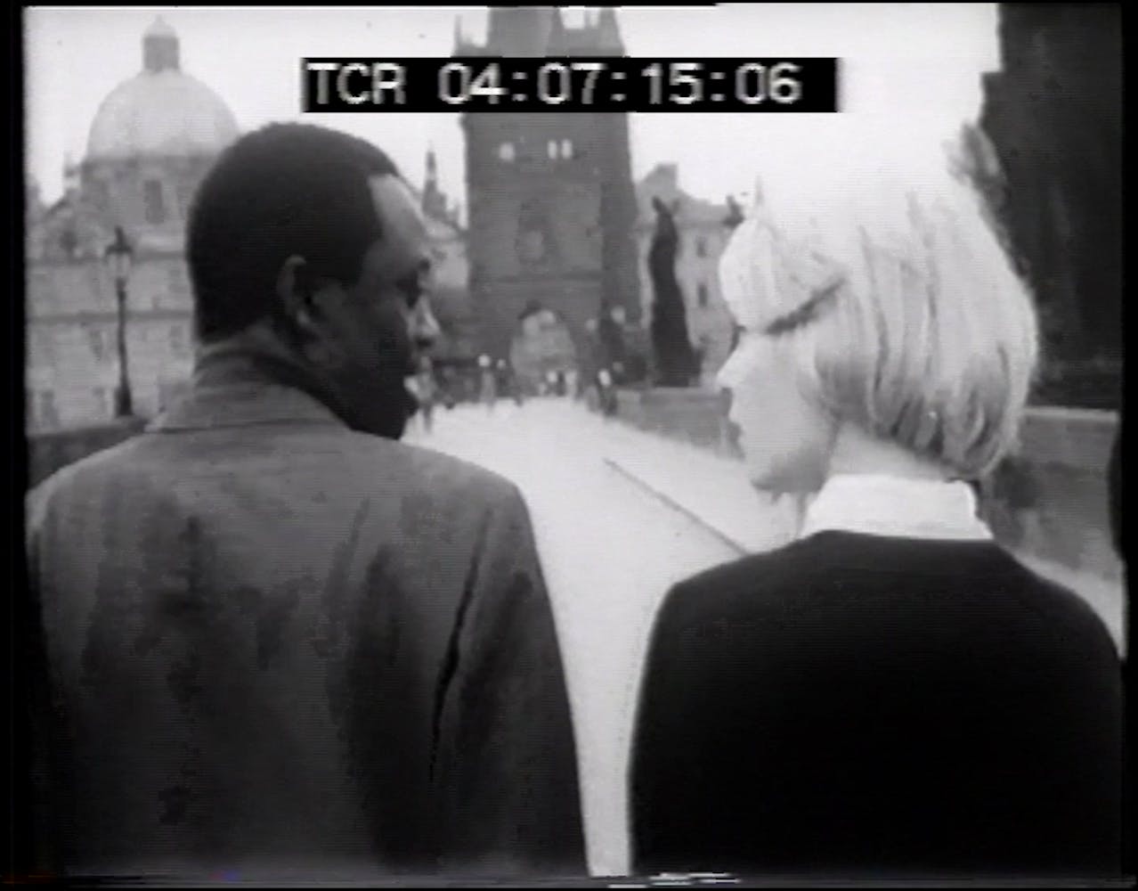 A woman with light skin and a man with dark skin walk down a street talking.
