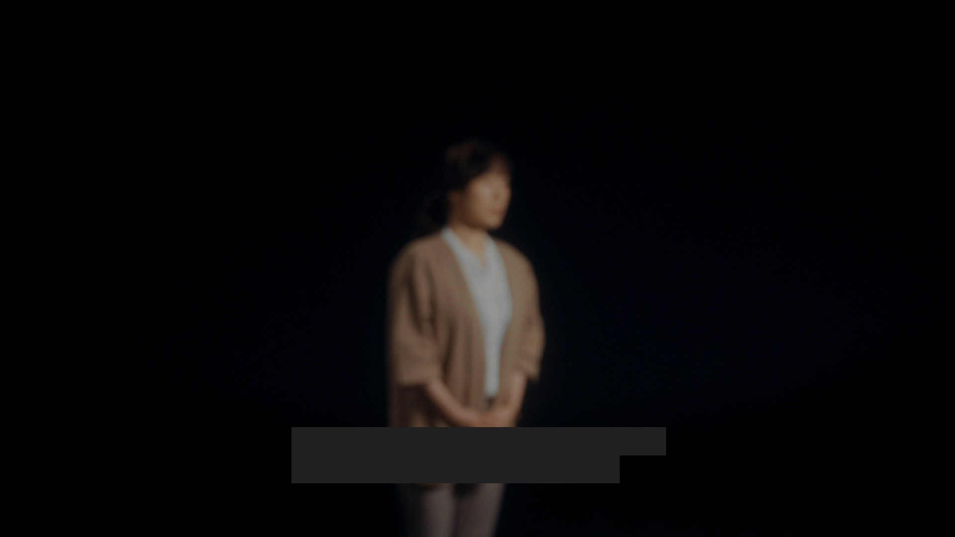 Blurry woman on black background with redacted text on bottom of image