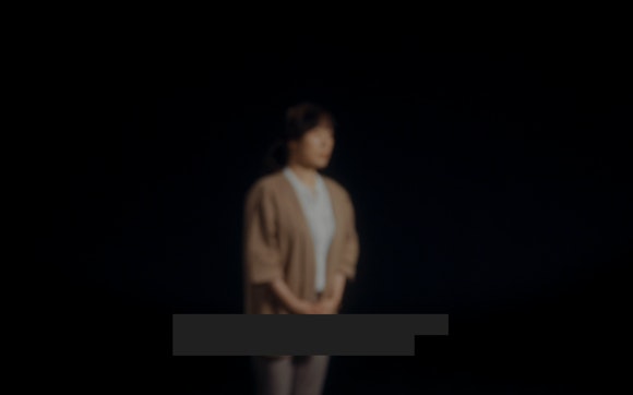 Blurry woman on black background with redacted text on bottom of image