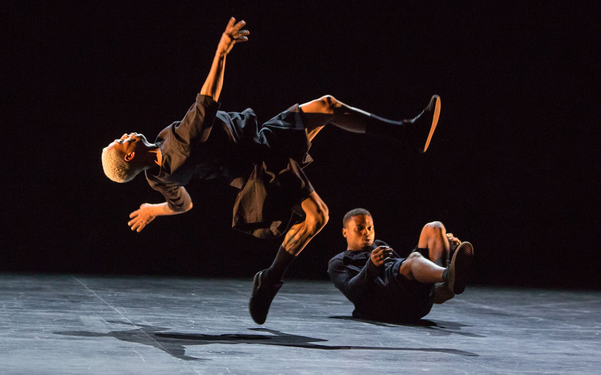 One dancer jumping in mid air and another dancer on the ground.