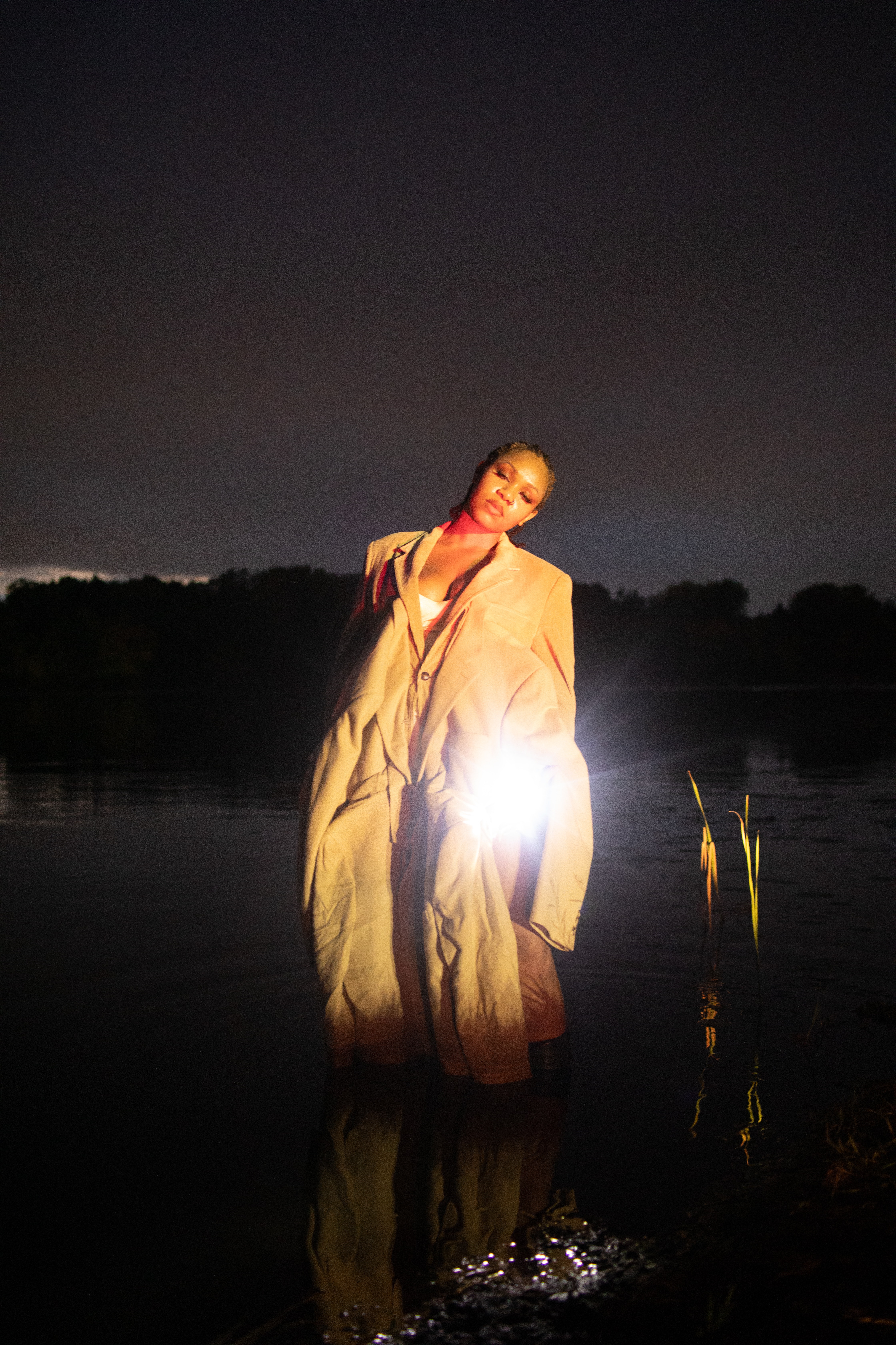 A person stands in a lake at night holding something glowing.