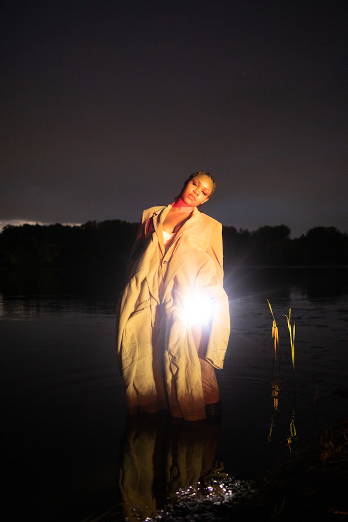 A person stands in a lake at night with their eyes closes and holding something glowing.