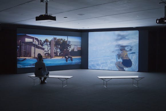 Image of gallery with two projections on dark wall and benches and visitor in foreground
