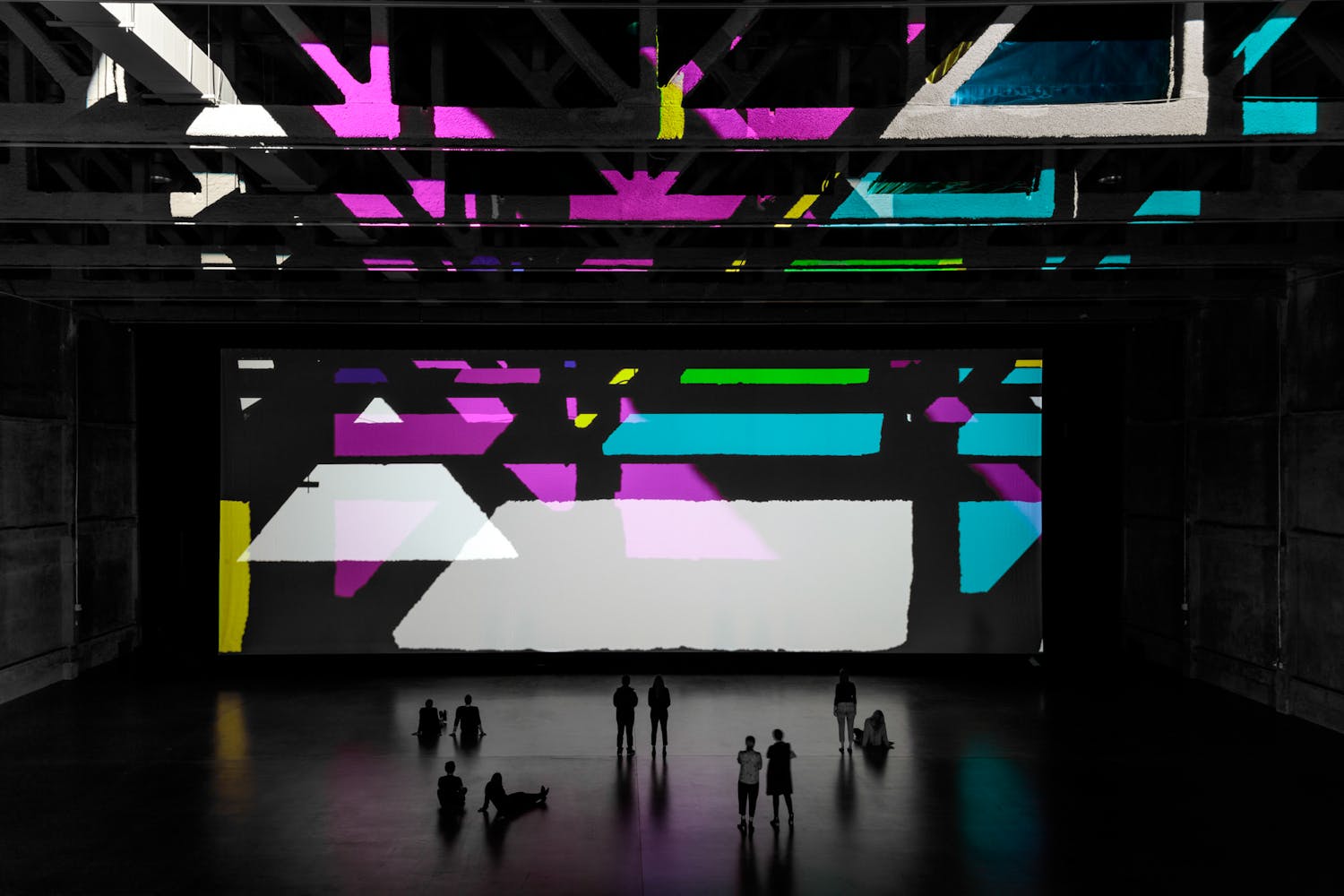 Image of large gallery with brightly colored geometric projections and visitors