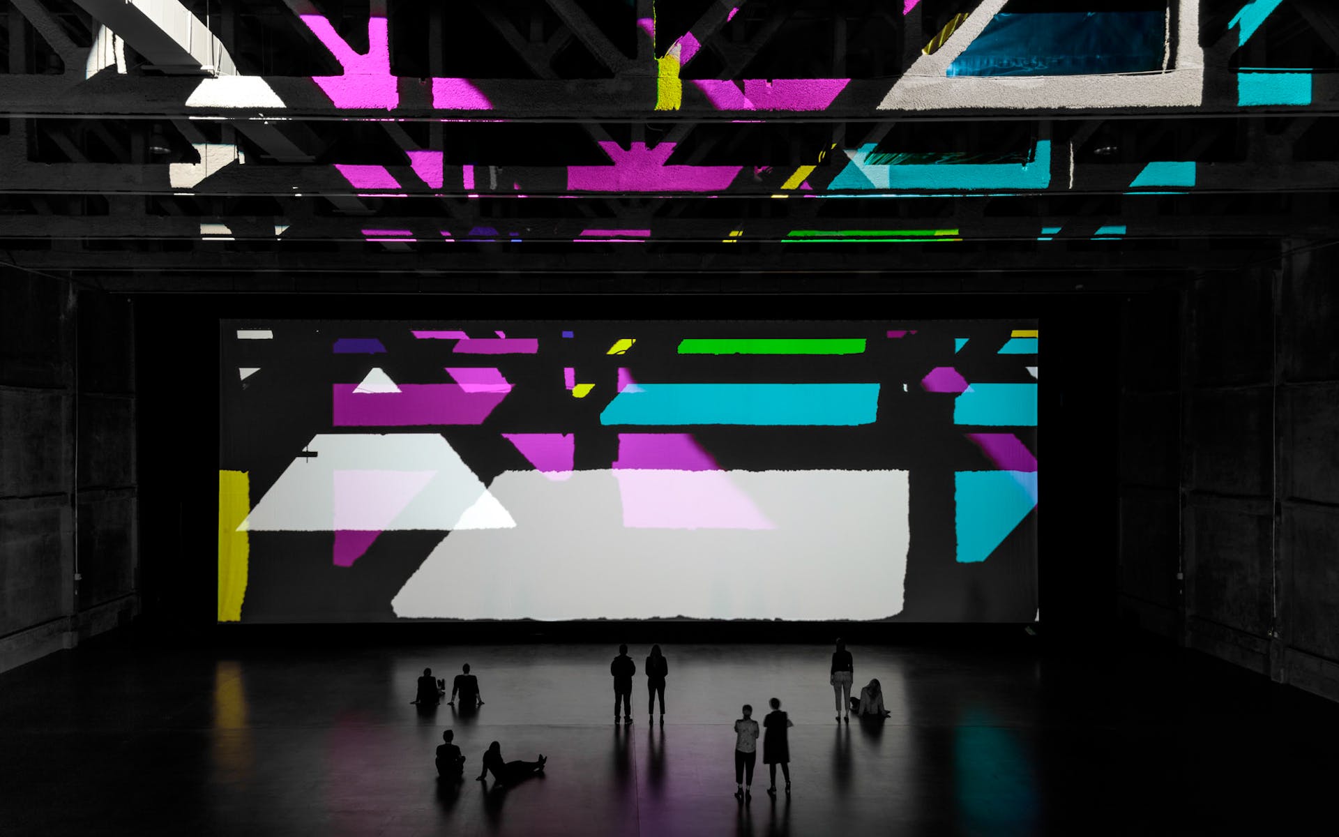 Image of large gallery with brightly colored geometric projections and visitors
