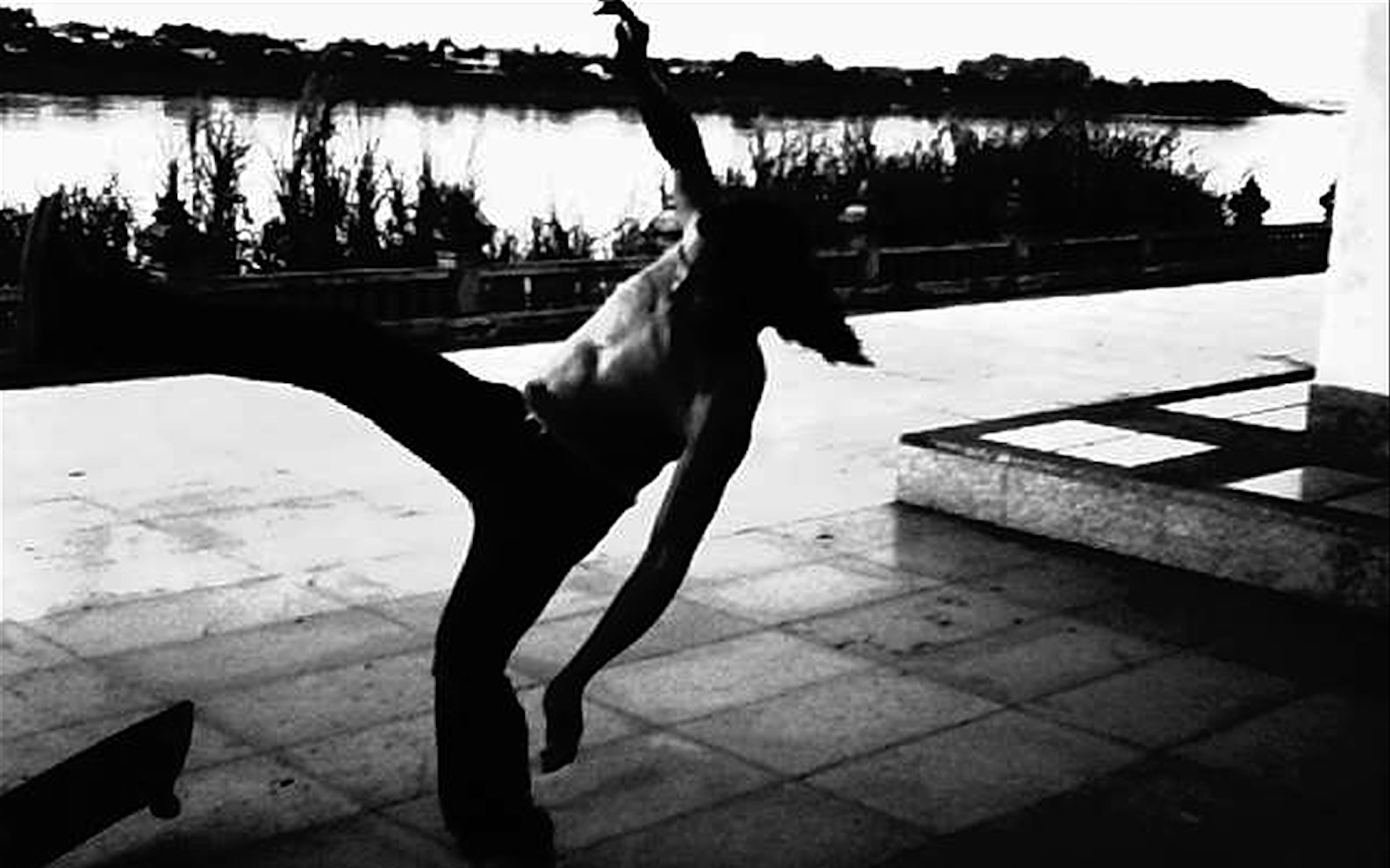 Cactus_River_Weerasethakul_18_PP A man kicks his leg up while standing outside.