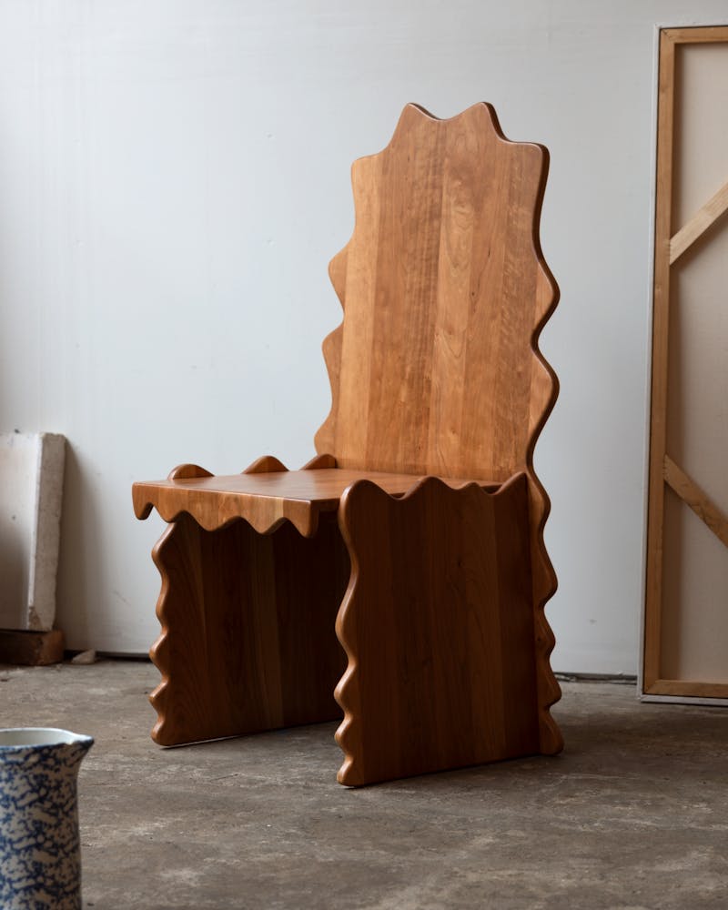 A wavey wooden chair sits in a studio.