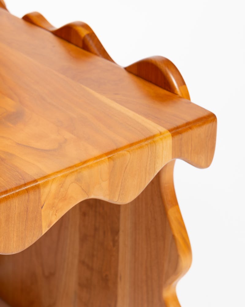 A wavy wooden chair sits in a white backdrop.