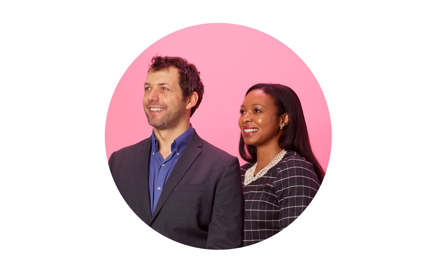 A light skined man and a dark skined woman stand next to one another looking up and away while smiling.