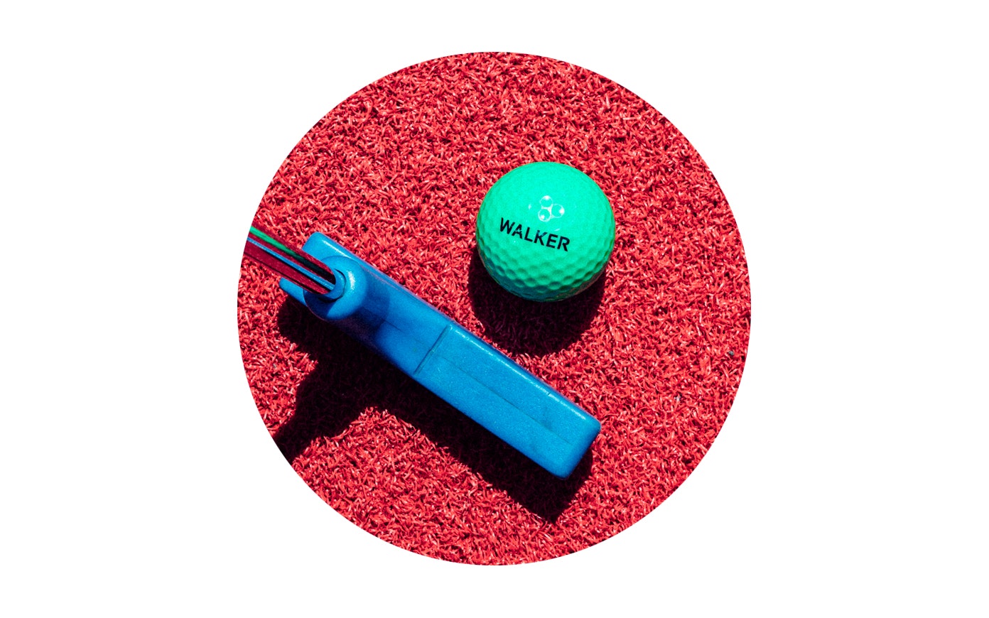 A green mini golf ball with the word "Walker" on it sits on red astroturf with a mini gulf club next to it.