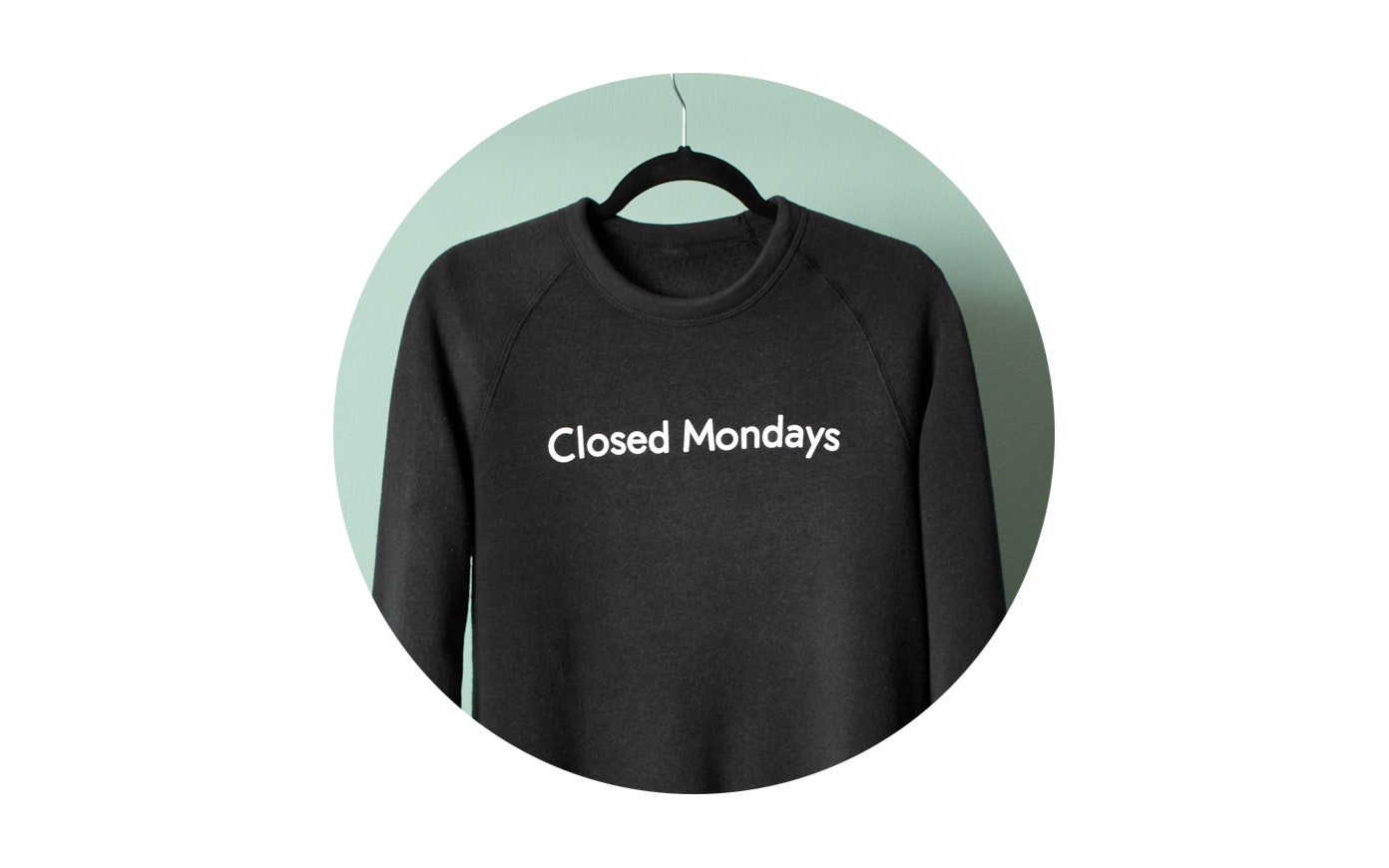 A black sweatshirt with "Closed Mondays" in white text on it hangs on a clothes hanger.