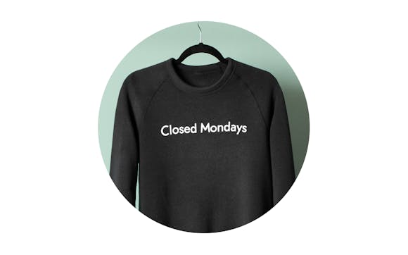 A black sweatshirt with "Closed Mondays" in white text on it hangs on a clothes hanger.