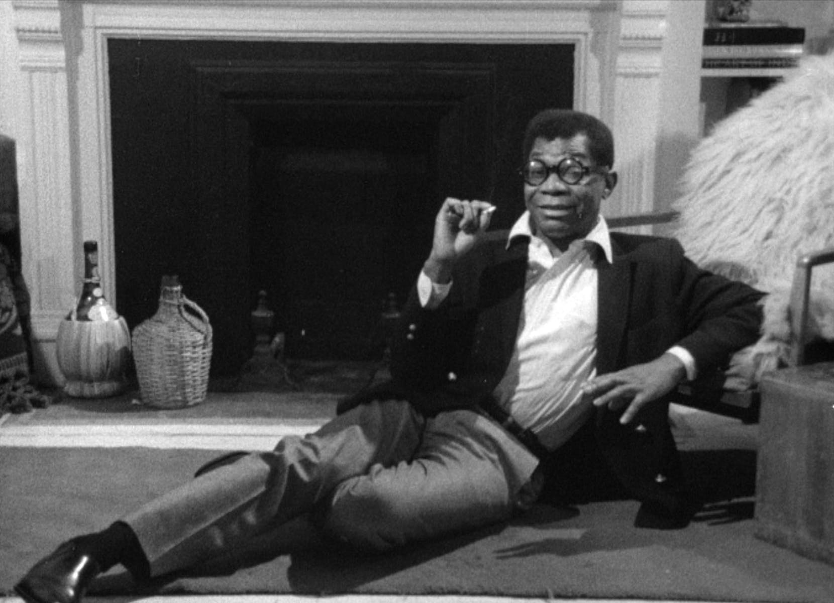 Image of man in suit lounging in front of fireplace