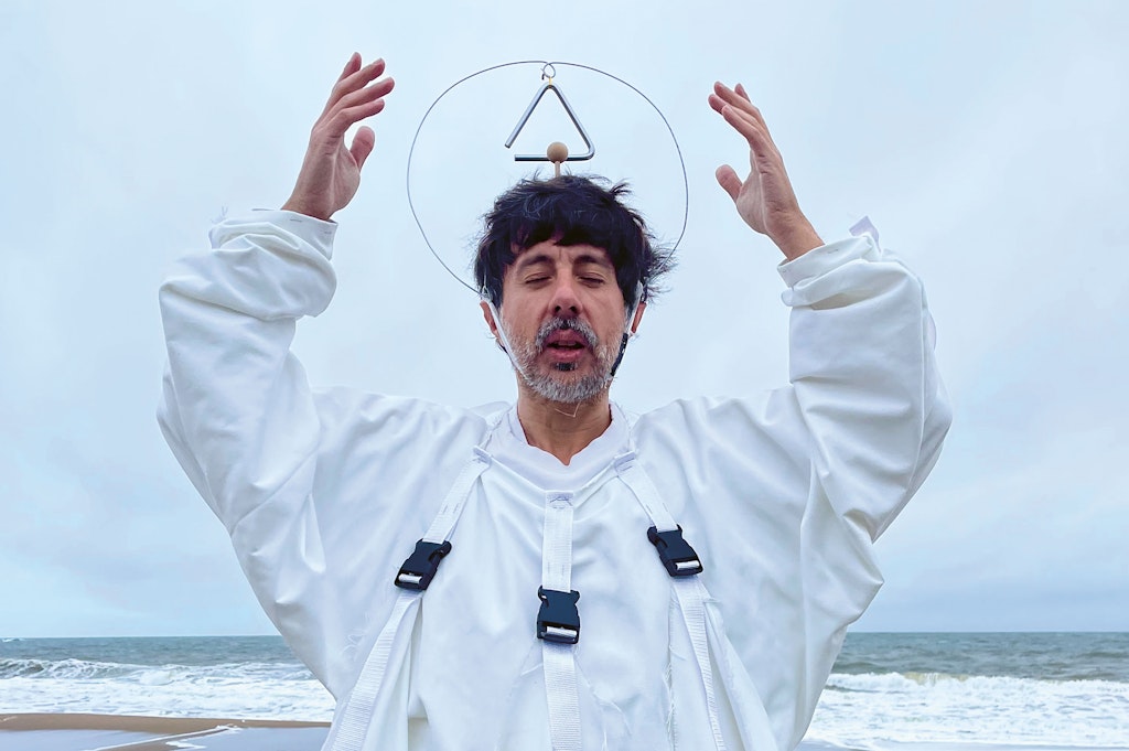 Locally Uploaded Image This image was uploaded directly to AltText AI for processing. A man in white robes poses on a beach with a triangle halo headpiece, raising his hands.