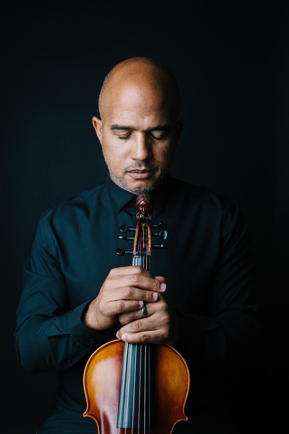 A dark-skinned man with his eyes closed holds a violin.