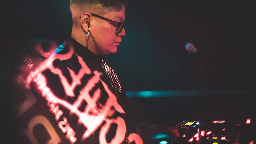 Profile of a medium-dark skinned adult wearing black glasses and red printed jacket.