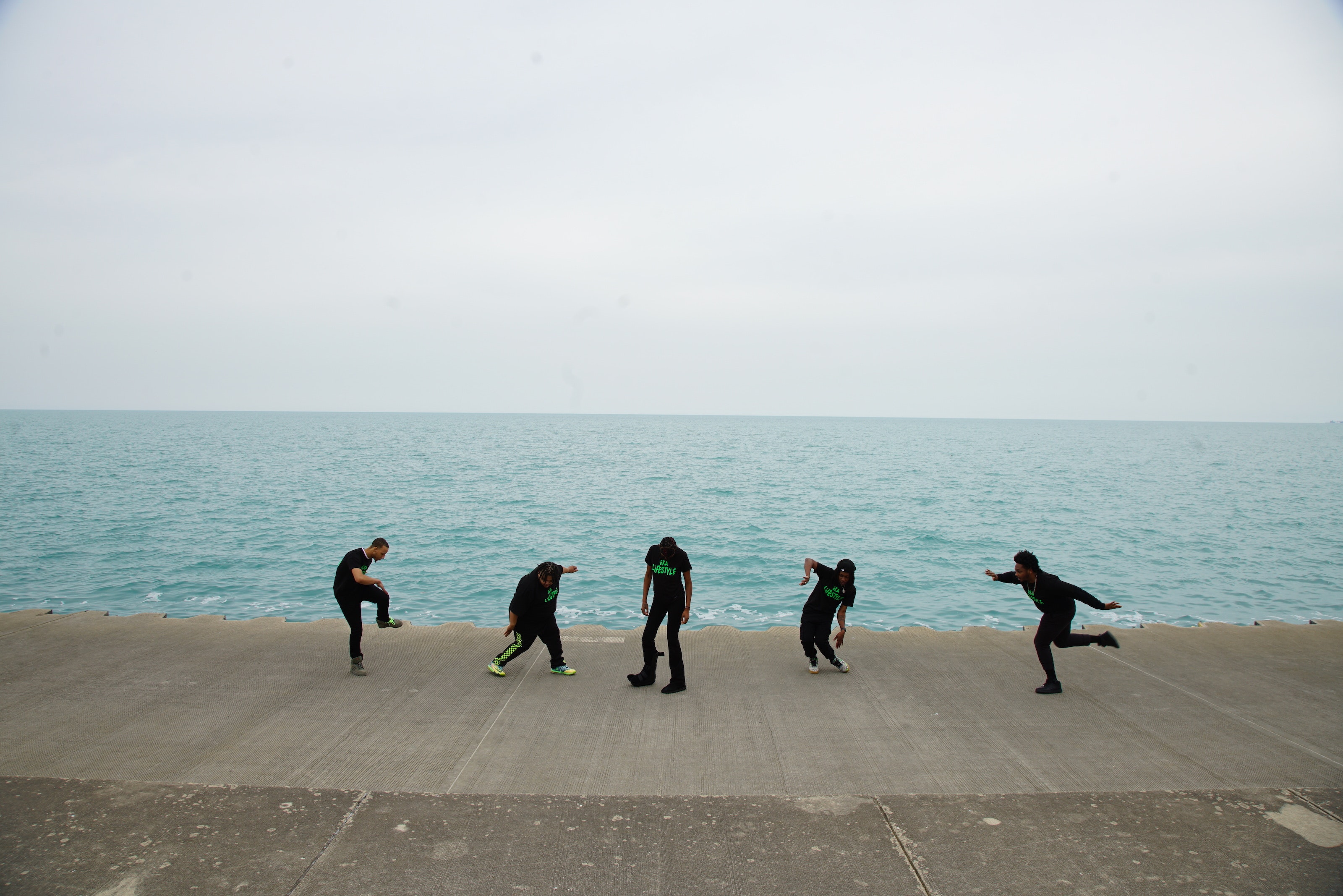 Image of five dancers on a concrete boardwalk with the sea in the background