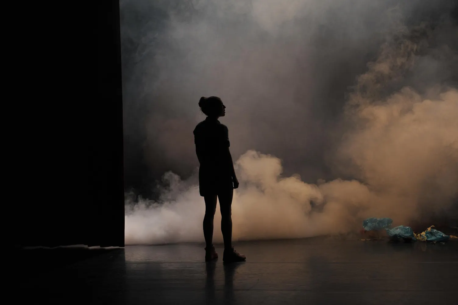 A woman stands in in front of smoke on a dark stage.