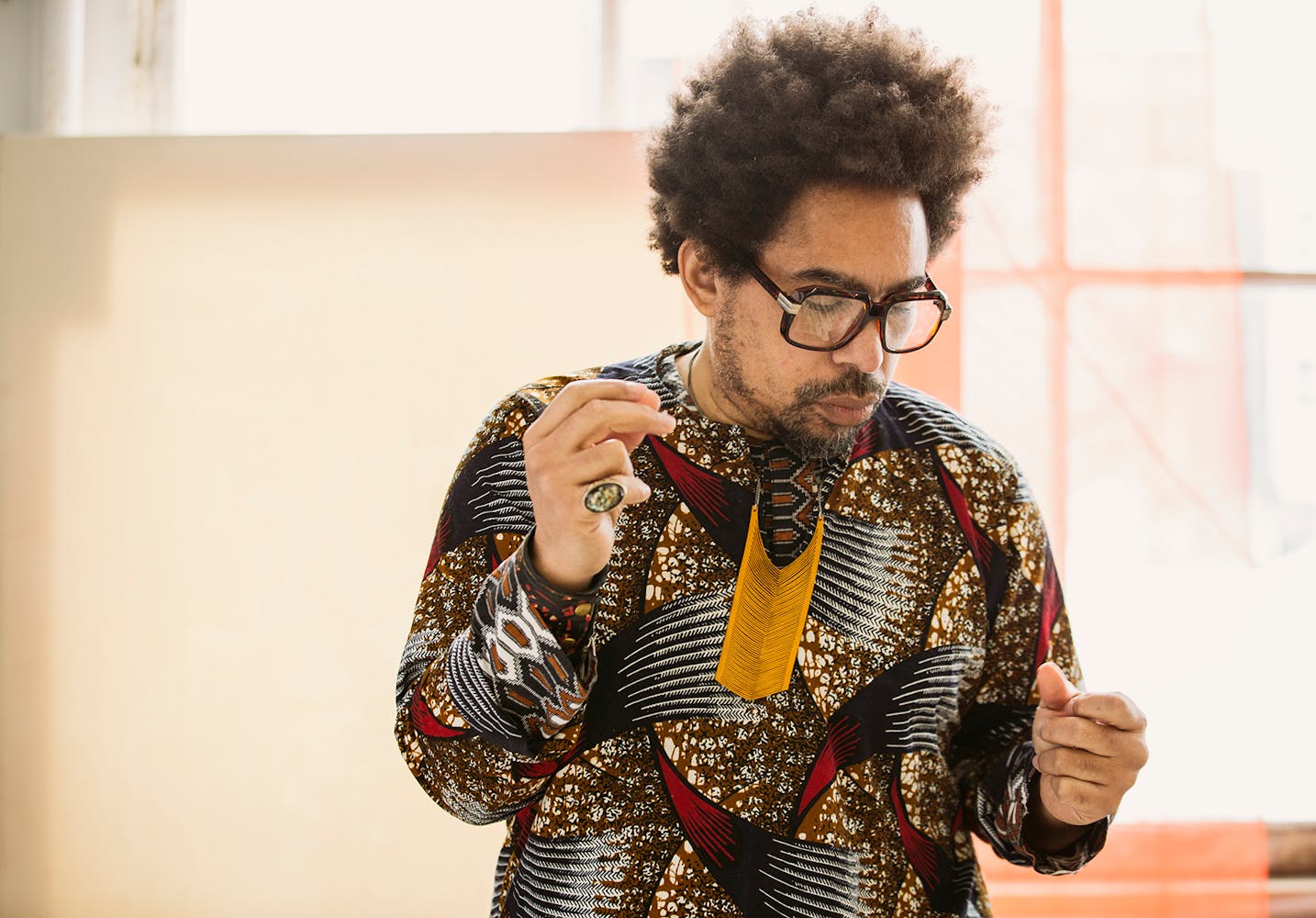 Damon Locks stands in a room with his arms in motion. He has an afro and thick-rimmed square glasses. It looks as though he is dancing or keeping beat.