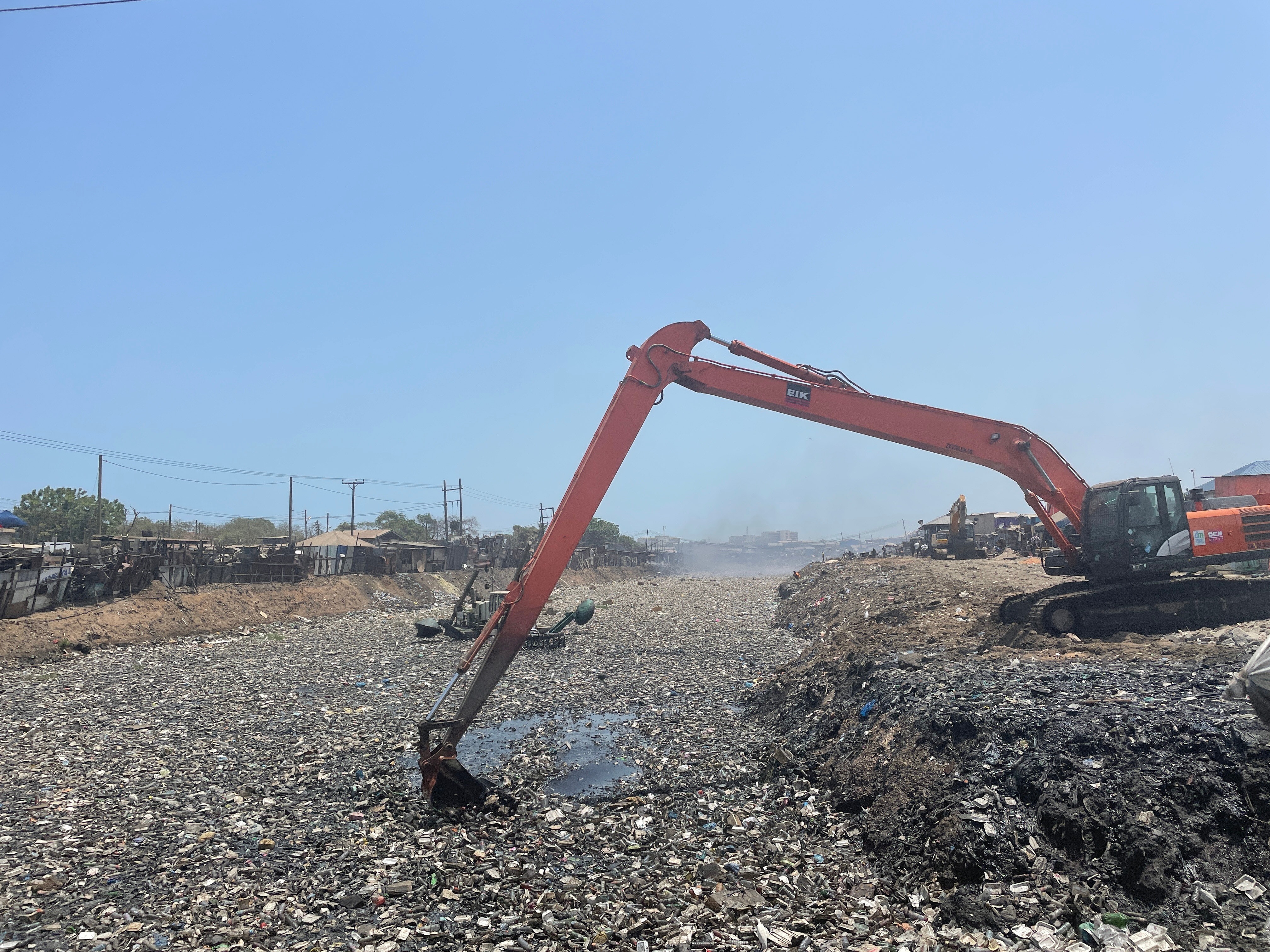 A large machine scoops electronics in an outdoor waste dump.
