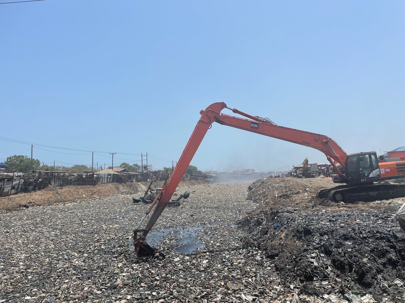 A large machine scoops electronics in an outdoor waste dump.