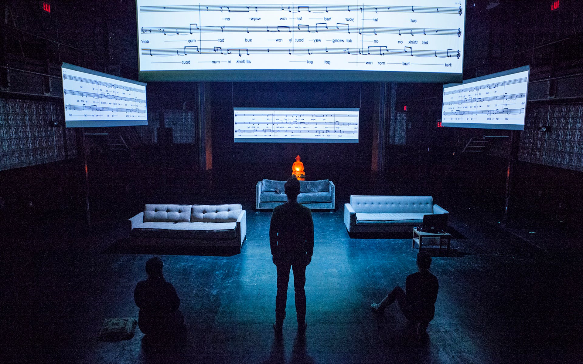 Silhouettes of three people standing and sitting under projections of sheet music.