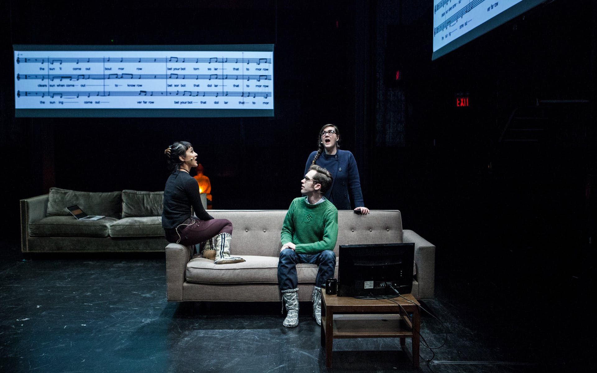 Three people sitting on a stage on a couch with musical notation projected in the background