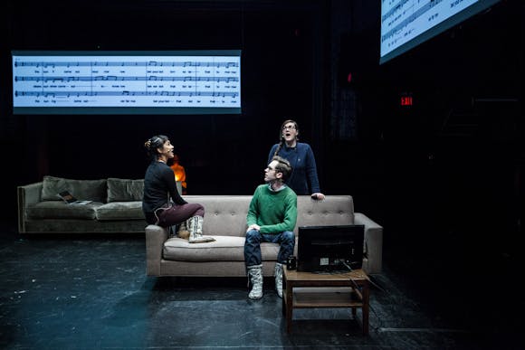 Three people sitting on a stage on a couch with musical notation projected in the background