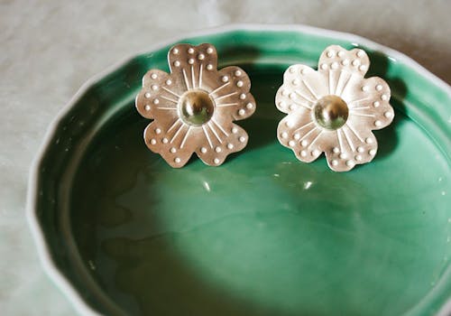 Image of flower shaped, metal earrings sitting on green ceramic dish