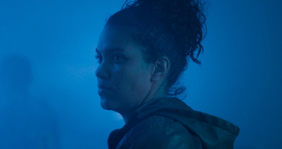 A woman looks over her shoulder while bathed in blue light.