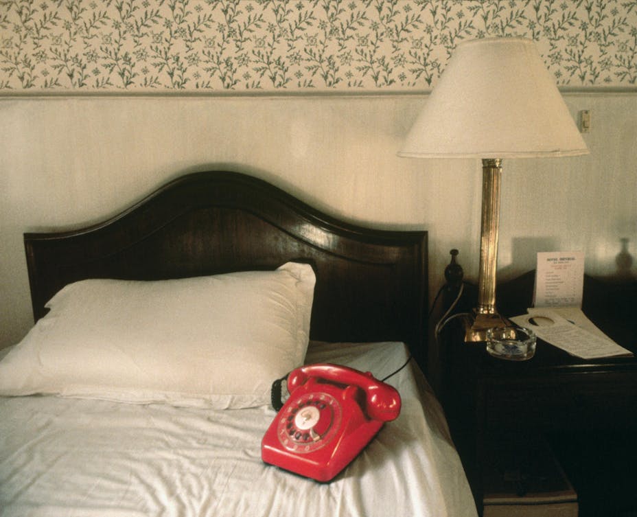 A red rotary telephone sits on a hotel bed.