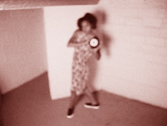 Blurry image of woman in corner holding what appears to be a clock