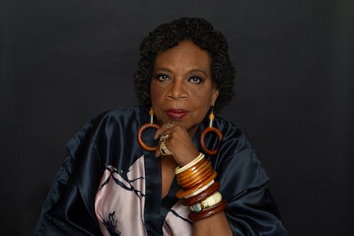 A musician with dark skin and wooden jewelry rests her head on her hand.