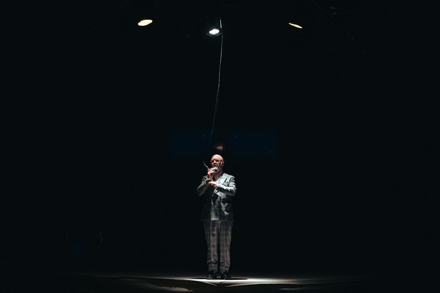 A performer with light skin speaks into a hanging microphone.