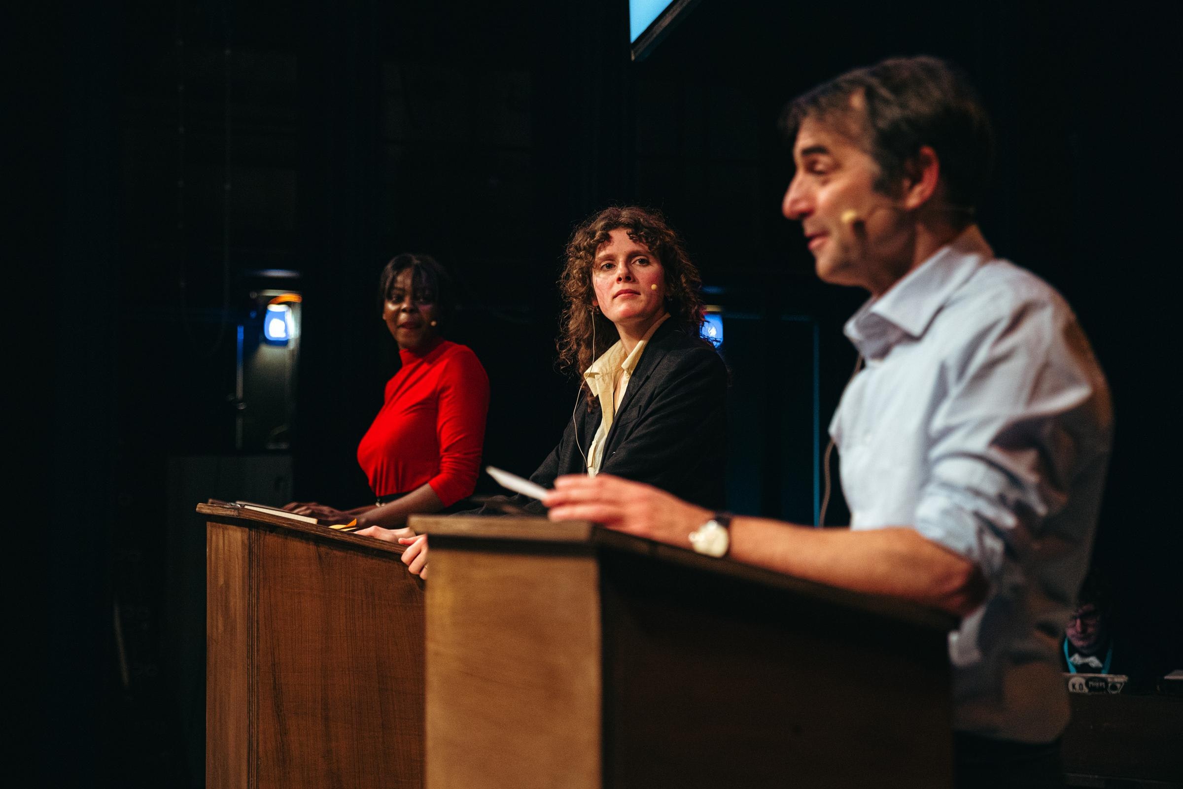 Three performers stand at three wooden podiums.