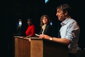 Three performers stand at three wooden podiums.