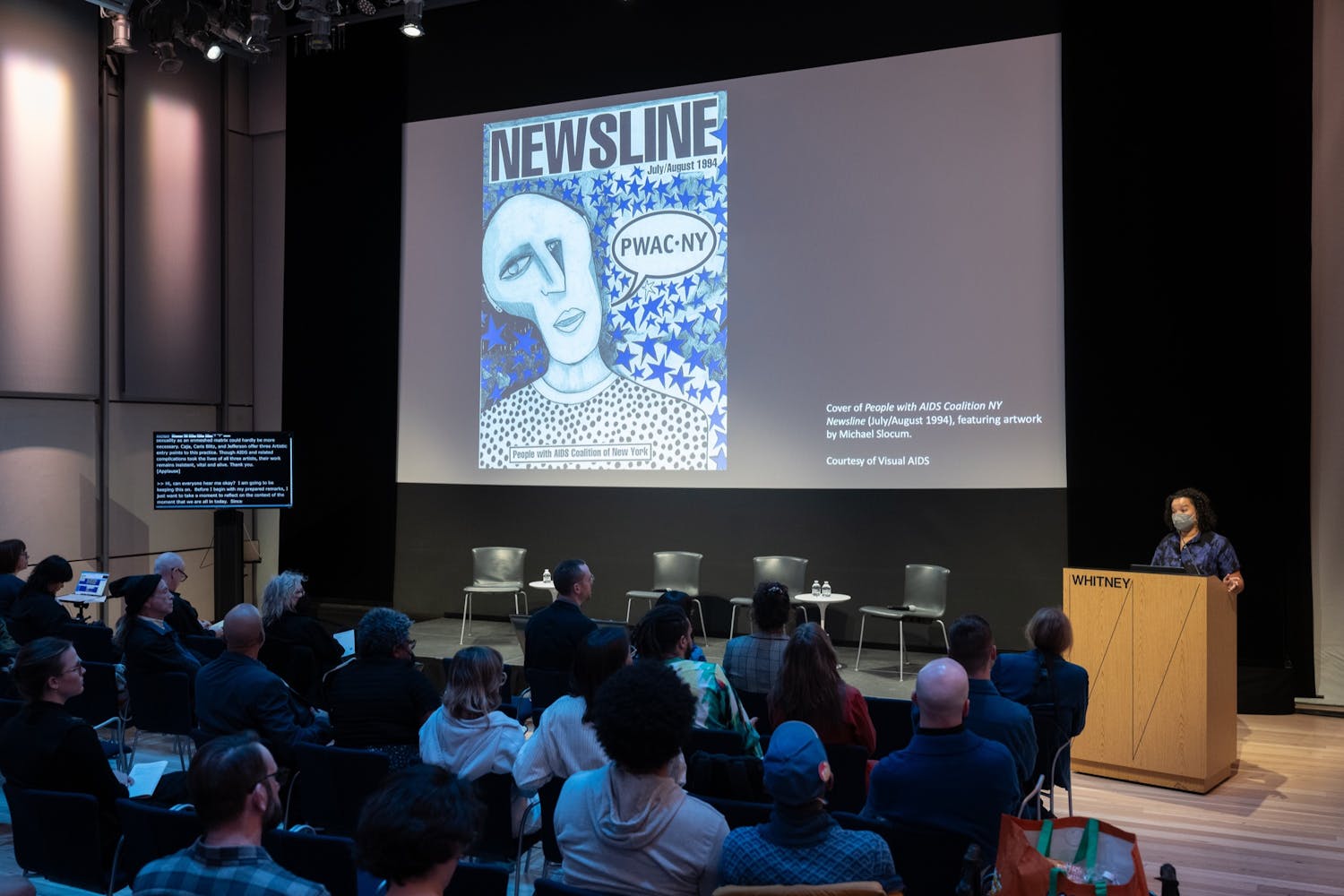A group of people listening to a person presenting, a projected images in a auditorium.
