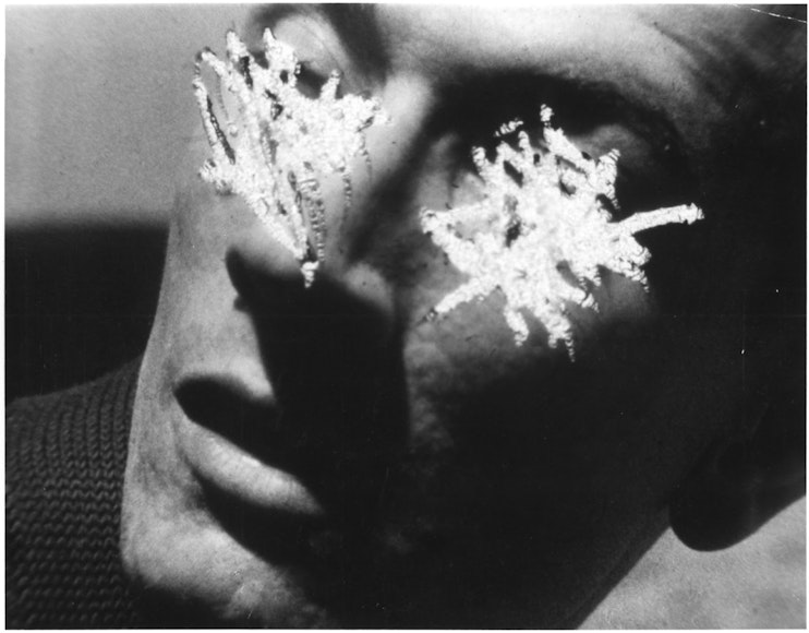 A black and white image of an adult with the eyes scratched out, leaving white marks on the photograph