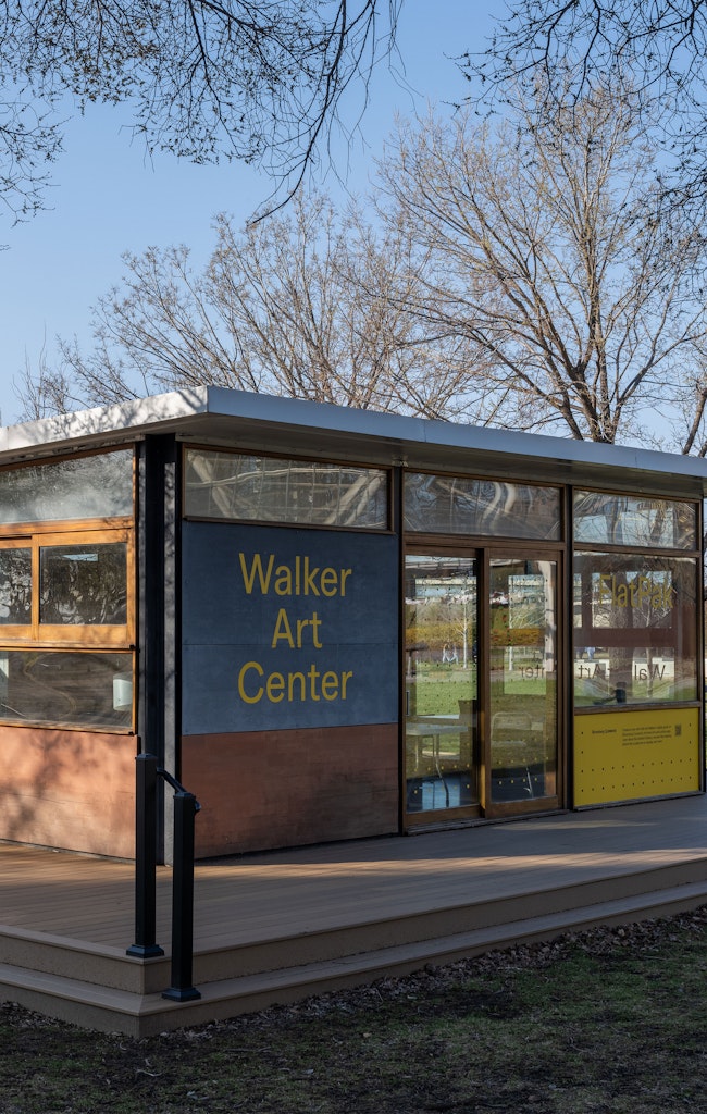 A square building with glass windows and a wooden deck. The front says Walker Art Center.