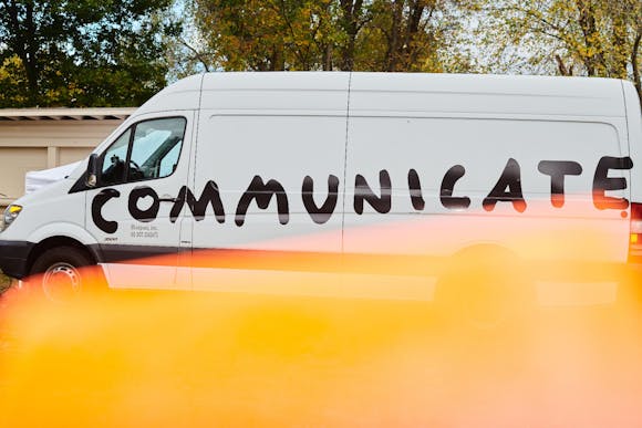 Image of white van with the word "Communicate" painted on it