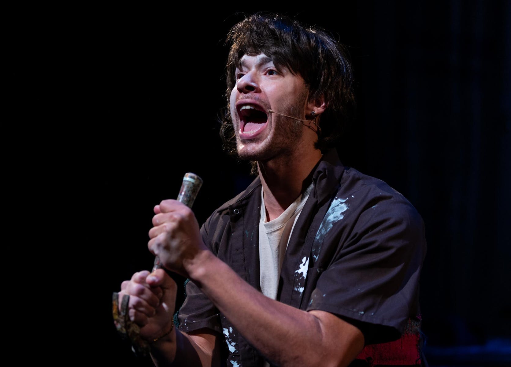 A performer with medium dark skin holds a hammer like a microphone.