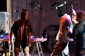 A performer with medium dark skin sneers at a puppet of himself.