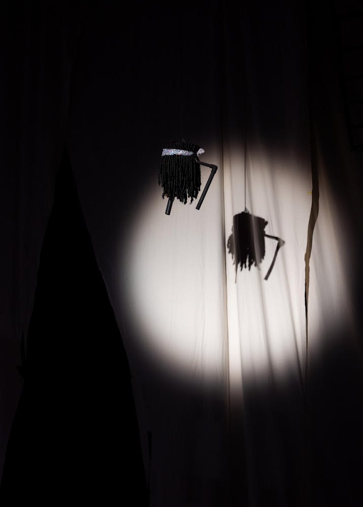 A dark colored wig with a bandana hangs from above.