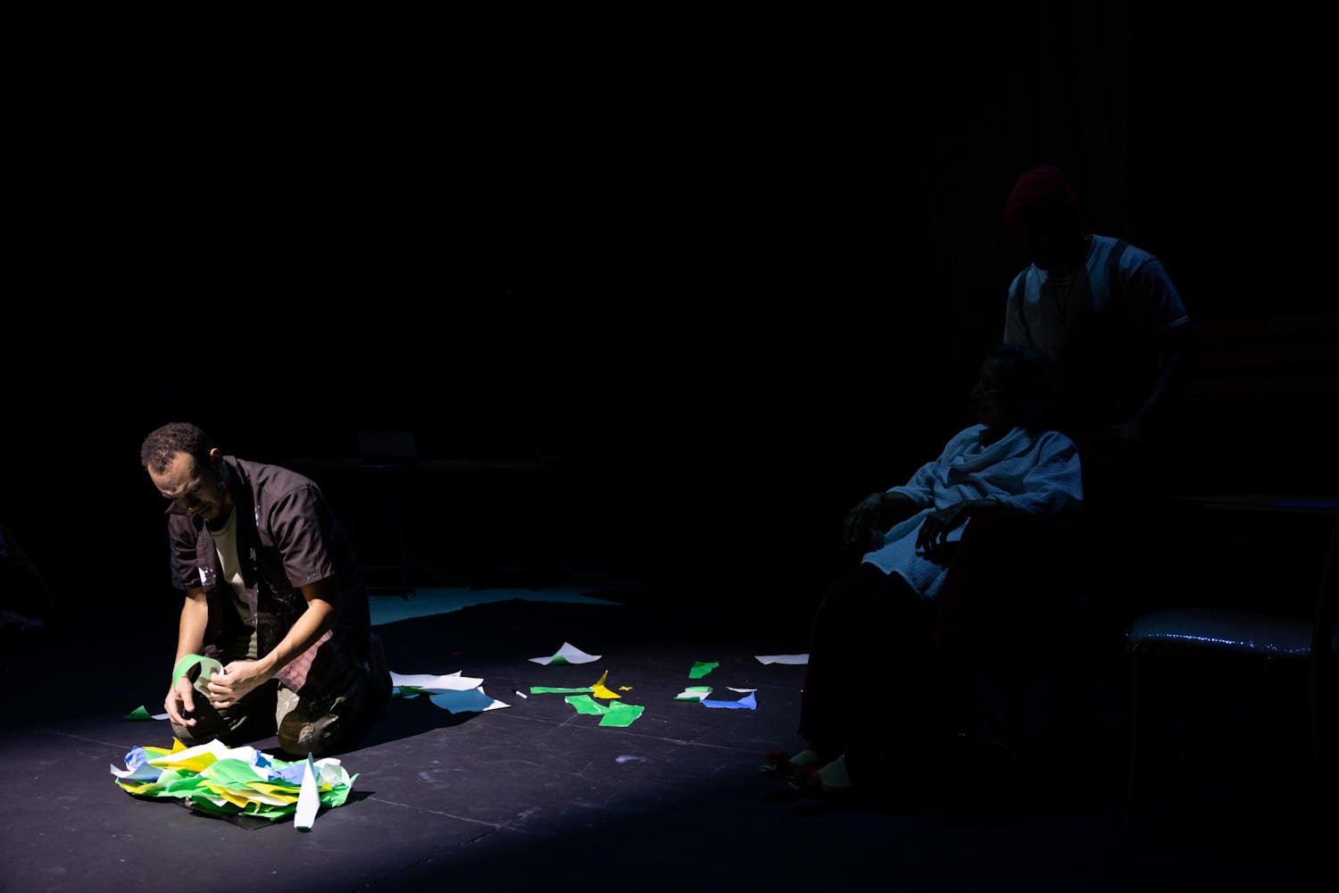 A performer with medium dark skin picks up colored paper scraps off the ground.