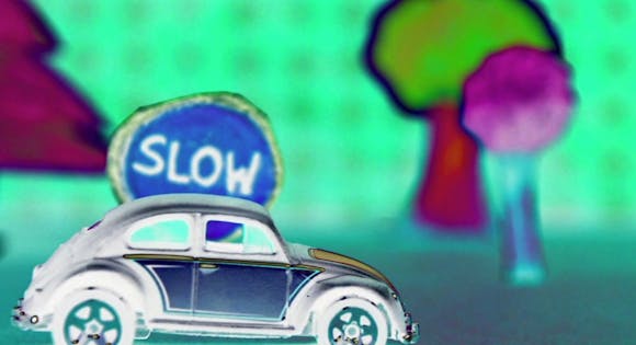 Film still animation of car in foreground with trees and "SLOW" sign in background