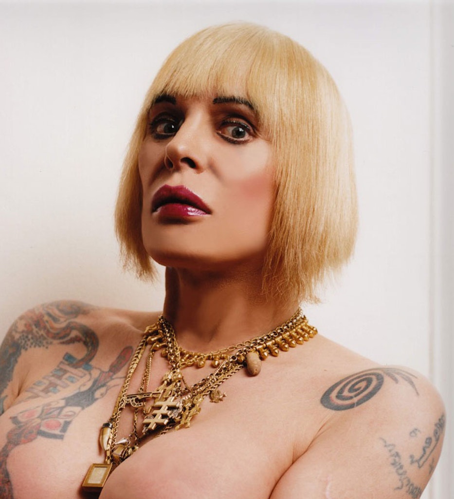 An adult cups their breasts in their arms and looks at the viewer.